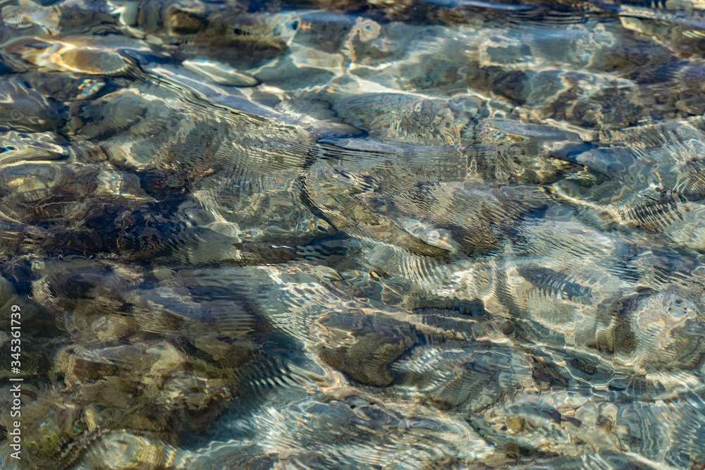 The surface is salty sea water, swaying in small waves near the shore, through the transparent bottom you can see stones and pebbles
