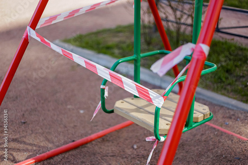 The playground is in quarantine due to the coronavirus pandemic. Warning Red and white ribbons are torn by bad citizens on a swing.