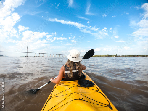 Young woman with fisherman's hat kayaking in Paraná river. Water active sports.