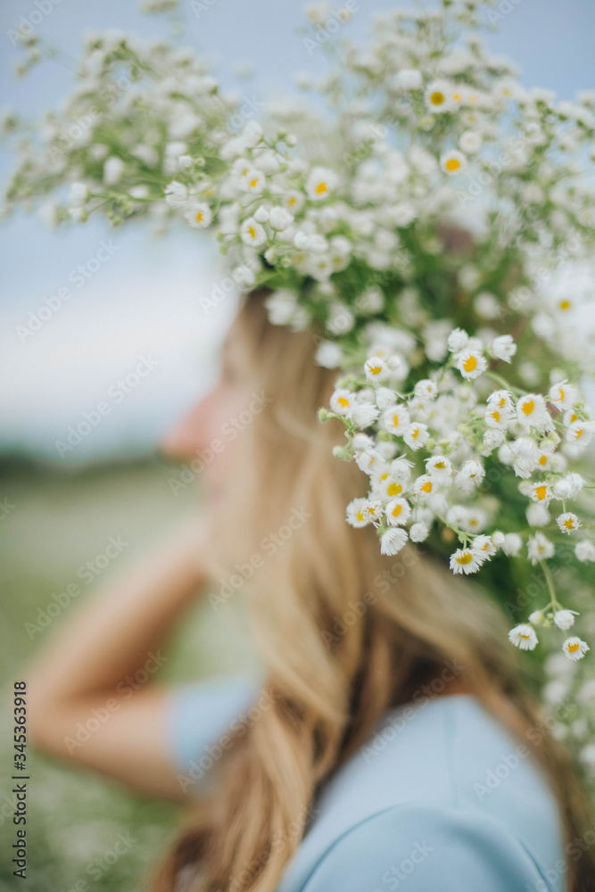 Naklejka premium beautiful blonde girl in a field of daisies. wreath of wildflowers on his head. woman in a blue dress in a field of white flowers. charming girl with a bouquet of daisies. summer tender photo