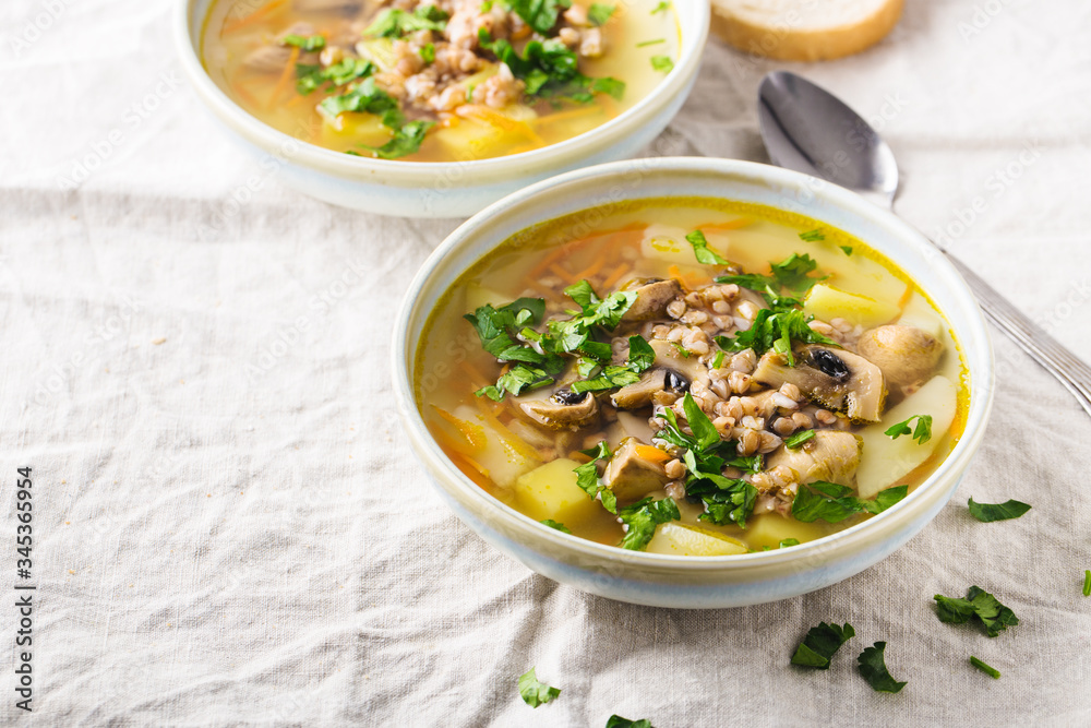 Soup of mushrooms, buckwheat, potatoes and carrots with herbs in bowls, light background, horizontal format. Copy space