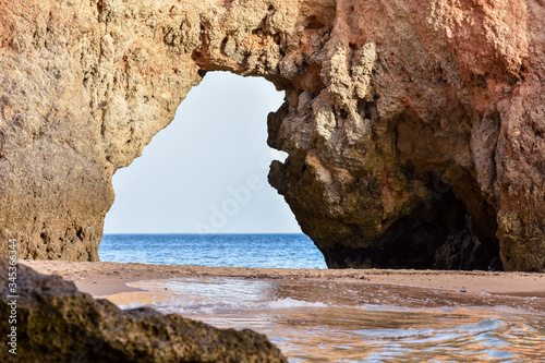 Empty beach between cliffs and natural archway through which you can see the sea. Uncrowded travel concept. Algarve, Portugal. Algarve, Portugal