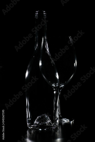 Empty transparent bottle silhouette with wine glass behind. The background is black