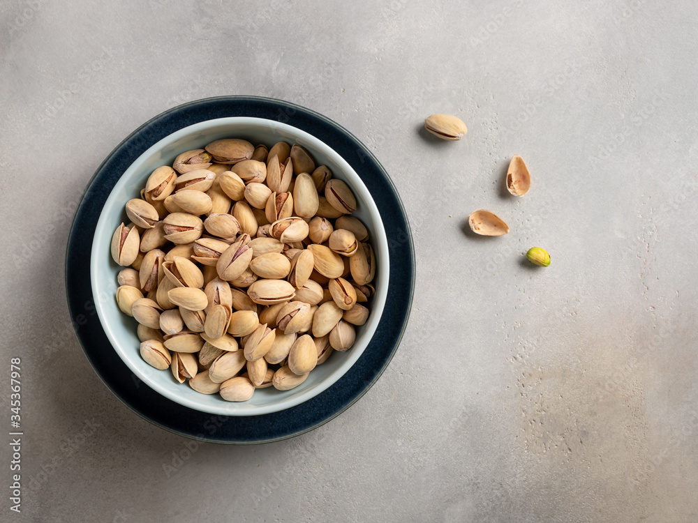 pistachios in a blue bowl on a gray beige background. healthly food. top view with space for copy.