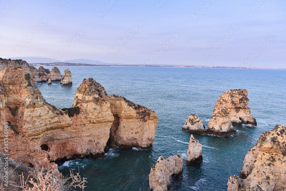 Cliffs of orange colored rocks and truqeussian waters. City of Lagos in the background. Concept of tourism and travel. Algarve, Portugal