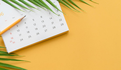 close up top view on white calendar 2026 with pencil and tropical leaves on yellow table background for planning work and life balance in holiday summer concept