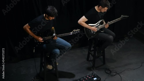 Two male guitarists in black clothes performing song in dark room. photo