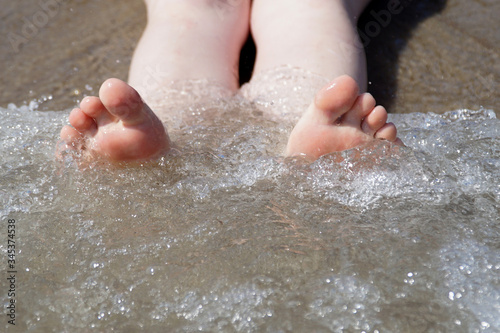  Female legs lie on the sand and washed by the wave.