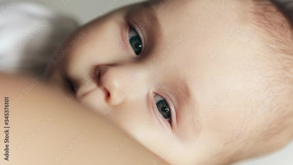 Close-up portrait of peaceful sleepy baby boy in mother arms. Baby looking on the camera.