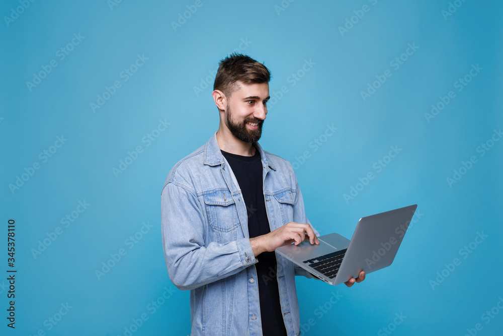 Young cheerful man with laptop in his hand. Guy browsing internet on computer and expresses happiness. Blue background. Free space for text.