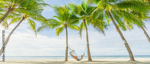 Woman lying on hammock between palms on the beautiful tropical beach. Travel and vacation concept. Banner and panoramic edition.