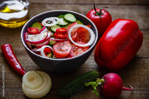 Salad of tomatoes cucumbers onions radishes avocado peppers on a wooden background.