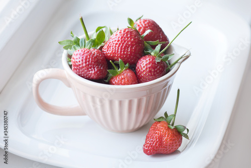 Strawberries with stalks in a ceramic cup on a white background, horizontal frame