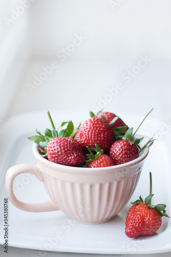 Strawberries with stalks in a ceramic cup on a white background, vertical frame