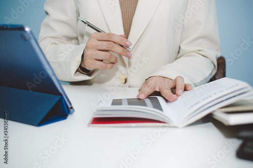 attractive businesswoman in white suit working and calculating about finance with, document report and digital mobile tablet on desk at office, digital online marketing and financial business concept