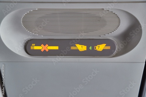 Photography Interior of a plane, ovehead panel with seatbelt and no mobile devices sign
