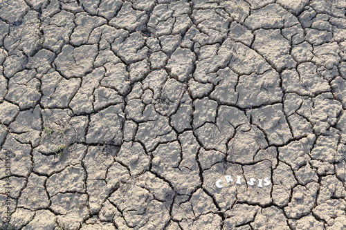 The word CRISIS in paper letters on the background of dry earth with cracks. Crisis concept.
