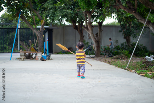 Back portrait of little boy carrying a broom and walking along the cement way