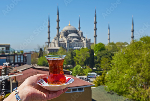 Woman's hand holding cup with Traditional turkish tea in front of Blue mosque aka Sultanahmet Camii in Istanbul, Turkey.