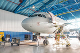 Airplanes under repair in a maintenance hangar. View of the nose and cockpit, open front door with a technical staircase.