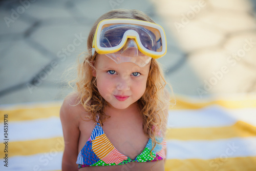 Little blonde girl with blue eyes in yellow swimming glasses sunbathing in the pool in the summer