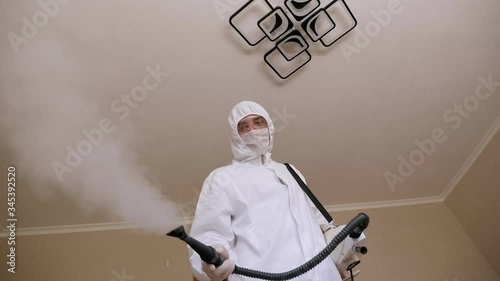 A man in a protective suit makes disinfection and decontamination from the coronavirus in the apartment with hot steam. Medical concept. Coronavirus disinfection. photo