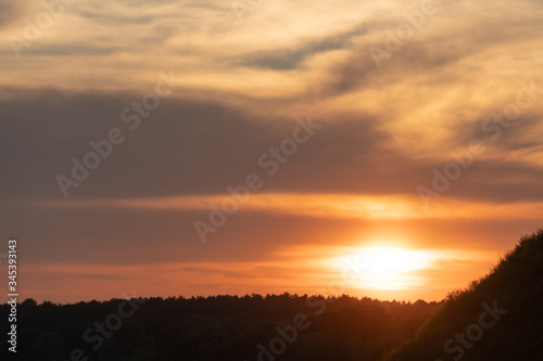 white and gray clouds are illuminated by the bright light of the setting sun. The sun is already on the horizon. Sunset or sunrise over the forest