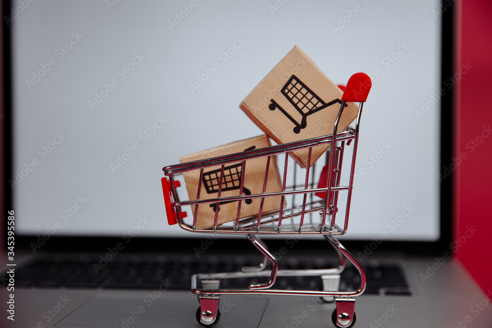 Online shopping concept. Laptop with mini market trolley and boxes.