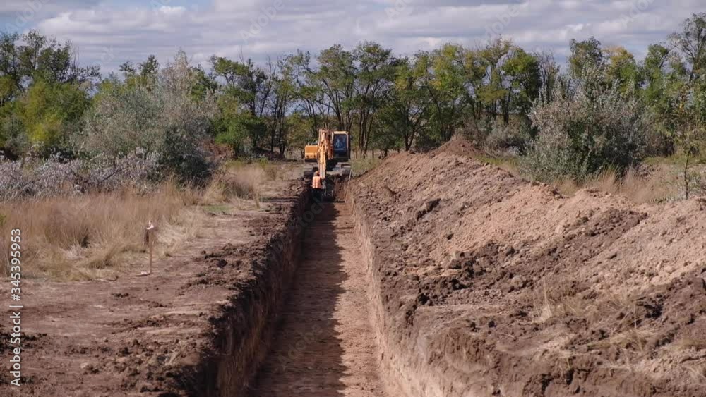 Excavator digs a long trench against the backdrop of beautiful nature