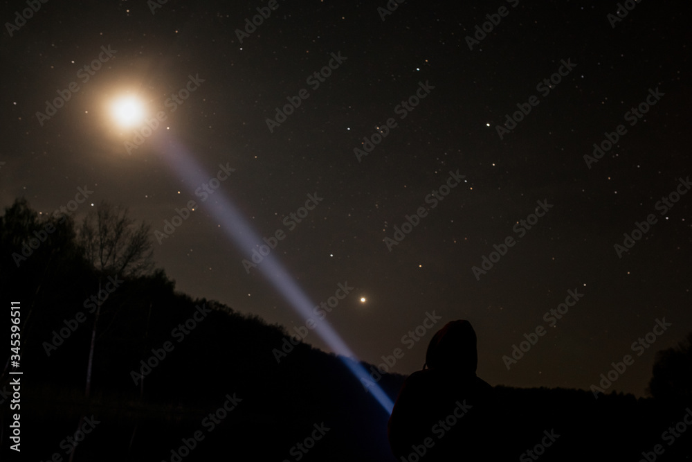 Man standing under the starry sky and shining a flashlight on the moon