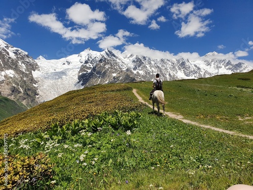 Man riding horse at the top of a pass in Svaneti region, Georgia.  Adishi Glacier of the Caucas mountain in behind. Beautiful summer day at the top of mountain. photo