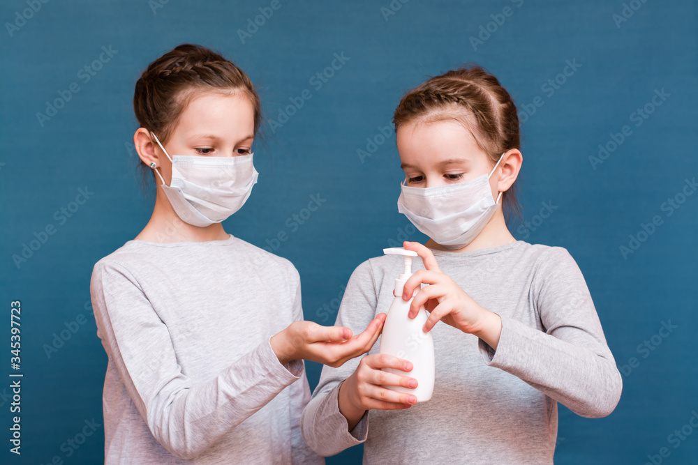 Covid-19 epidemic. Girls in medical masks treat their hands with a sanitizer on a blue background.