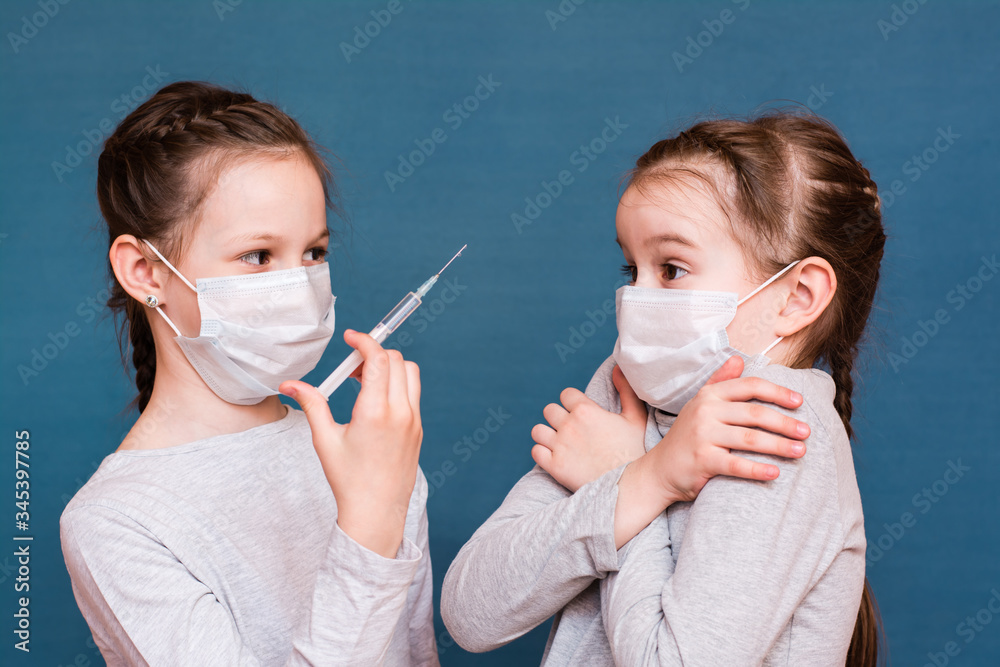 Girls in medical masks look at a syringe with medicine in hand. Vaccination, treatment of children. Outbreak Prevention