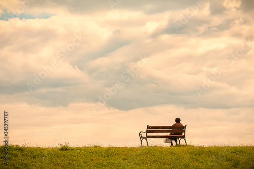 Pastel image. Horizontal frame. Line horizon and earth on a background of beautiful blue clouds. One woman sits on a bench and looks at the sea.