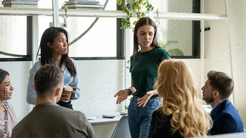 Confident female leader, mentor holding briefing for multiracial team workers in office, teaching students, plan to subordinates. Serious businesswoman at company meeting with mixed race colleagues.