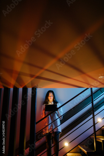 Woman using tablet computer while standing on a stairway indoors at home at night © 4Max