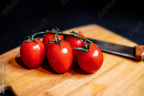 Cherry tomatoes lie on a chopping board with a vegetable knife. Ripe vegetables. Tomato set. Black background. Healthy nutrition. Vegetarian food. Healthy eating. The concept of product design. 