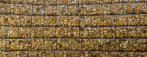 Wall made of gabions with stones. Stone wall with metal grid as background. Rock texture.