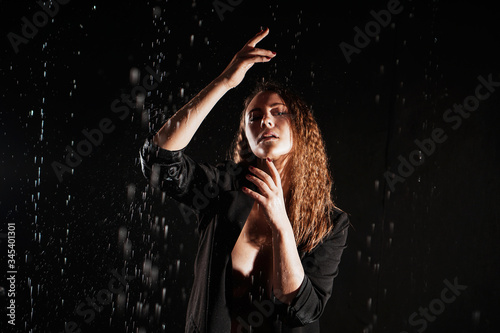 Wet beautiful woman in a black jacket under the falling drops of rain - photo in studio