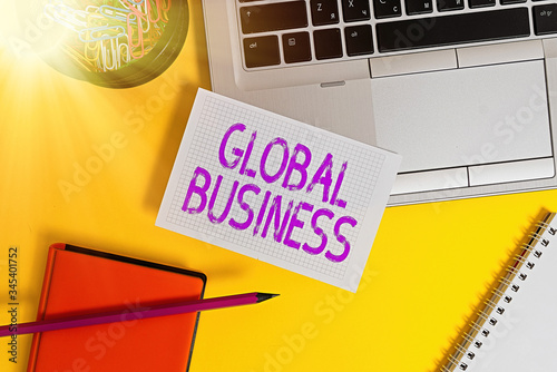 Text sign showing Global Business. Business photo showcasing Trade and business system a company doing across the world Laptop pencil sheet clips container spiral notebook colored background photo