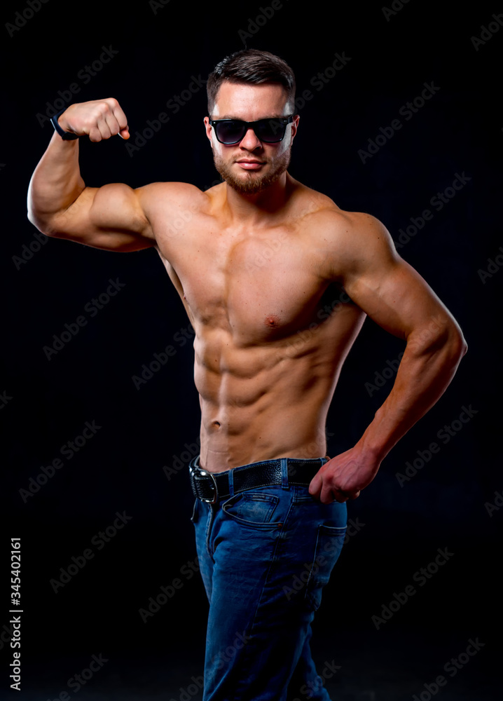 Strong brutal bodybuilder man with perfect abs, shoulders,biceps, triceps and chest showing his biceps. Blue filter on dark background