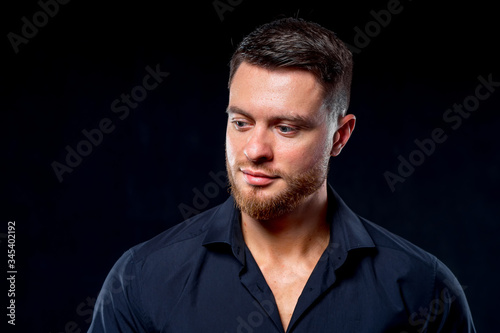 Young man in black shirt isolated on dark background. Portrait. Young male, bearded and athletic. Fashion portrait