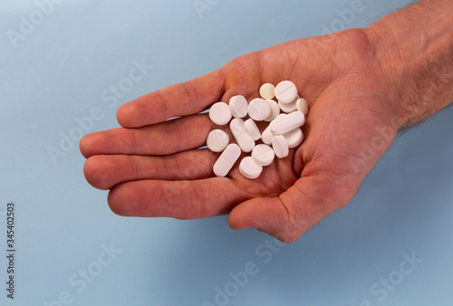 White pills in hand against a blue background. Medication at hand. Copy space for text.