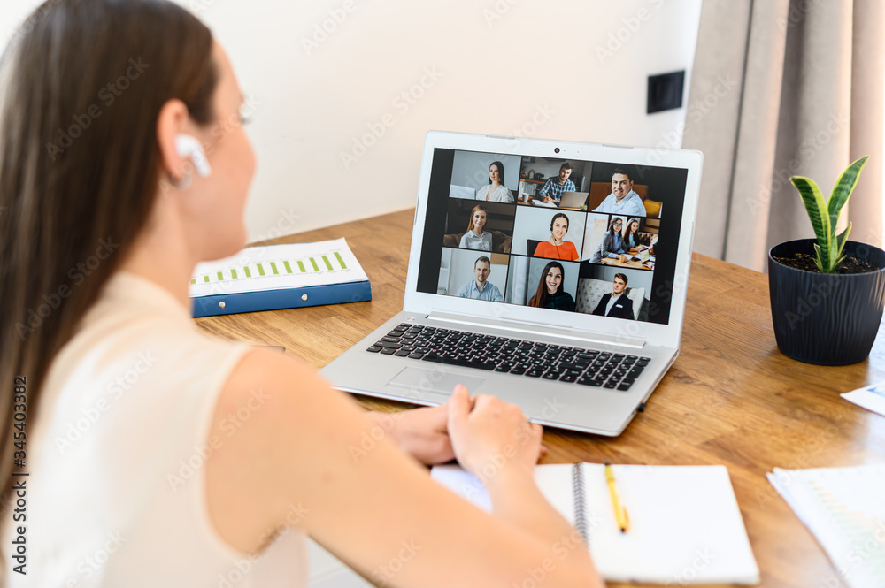 Virtual video conference, online meeting with a many employees together. A young woman is communicating via video call with coworkers, a several webcam shot of people on the laptop screen - obrazy, fototapety, plakaty 
