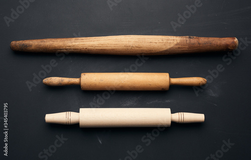 three types of wooden rolling pins for rolling dough on a black background