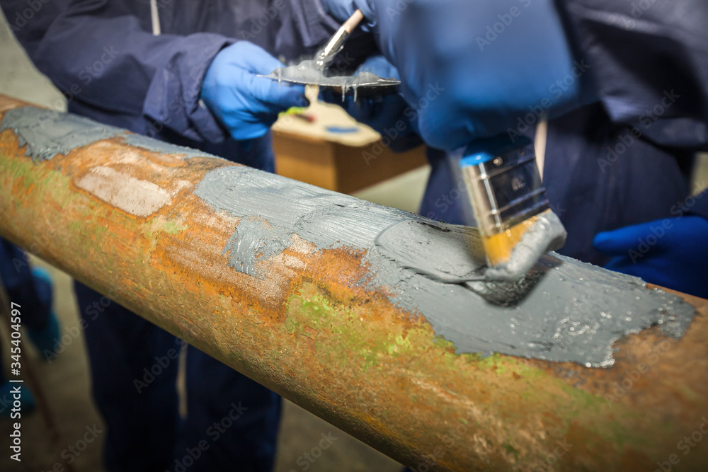 Restoration of the strength characteristics of the industrial pipeline. Resin coating on pipe. Hands and spatulas. Picture taken in Ukraine, Kiev region. Color image.