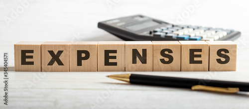 Expenses Word Written In Wooden Cube with pen and calculator