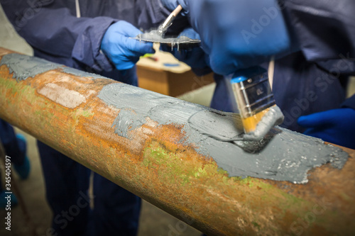 Restoration of the strength characteristics of the industrial pipeline. Resin coating on pipe. Hands and spatulas. Picture taken in Ukraine, Kiev region. Color image.