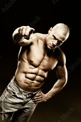 YOU are the TARGET! Portrait of strong healthy power fitness handsome athletic man with muscular trained body on black background pointing with finger to camera. Strength and motivation