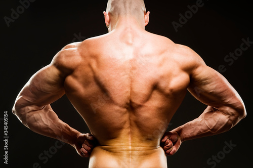 Body Builder Posing - Rear Lat Spread. Strong healthy power fitness handsome athletic man with muscular trained body flexing his lateral back muscle on black background